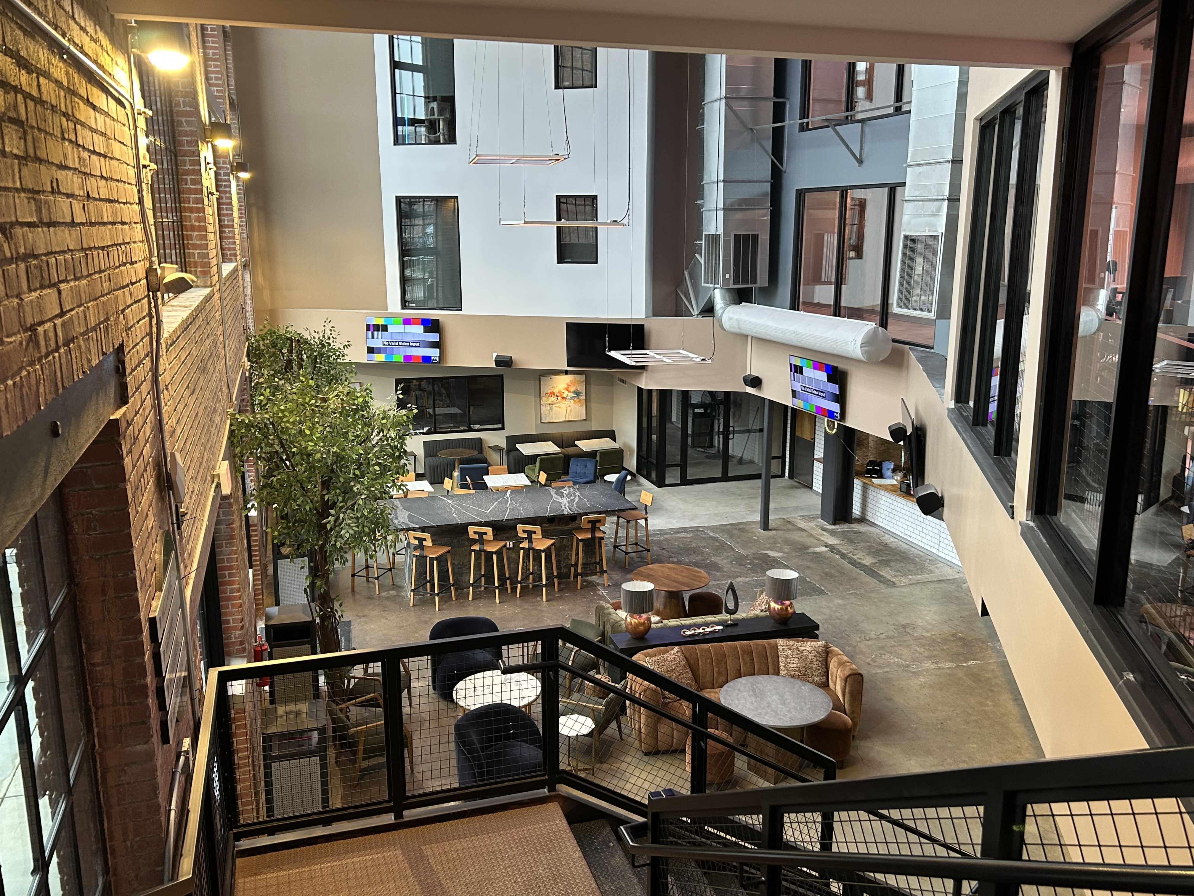 The Power House community lounge viewed from the staircase overlooking the full atrium, exposed brick walls, and seating area