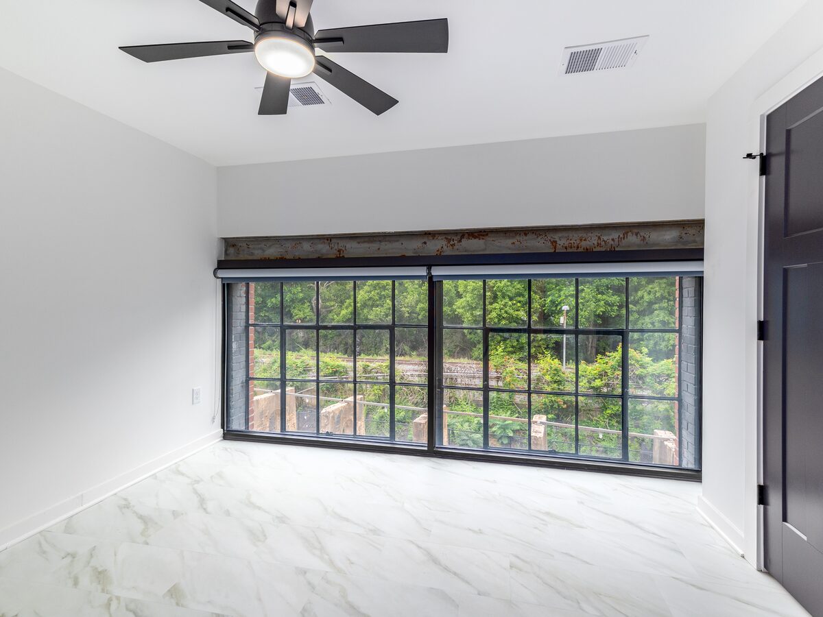 Spacious bedroom with original factory-pane windows overlooking a green courtyard at The Power House Apartments Rock Hill, SC